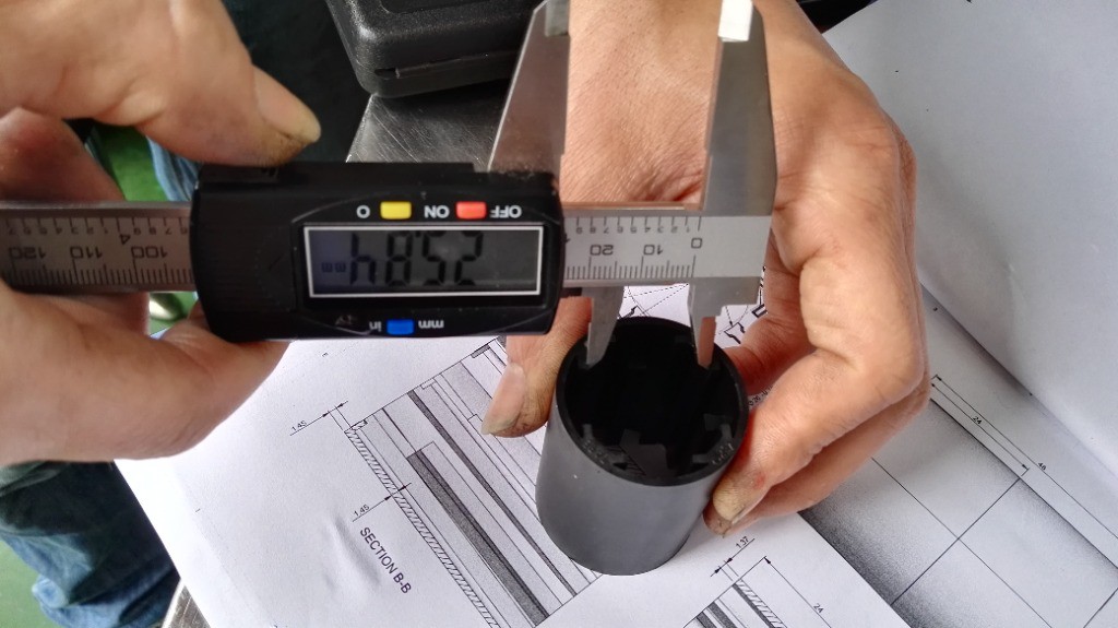 Technician measuring precision molded part with digital caliper against 2D engineering drawing